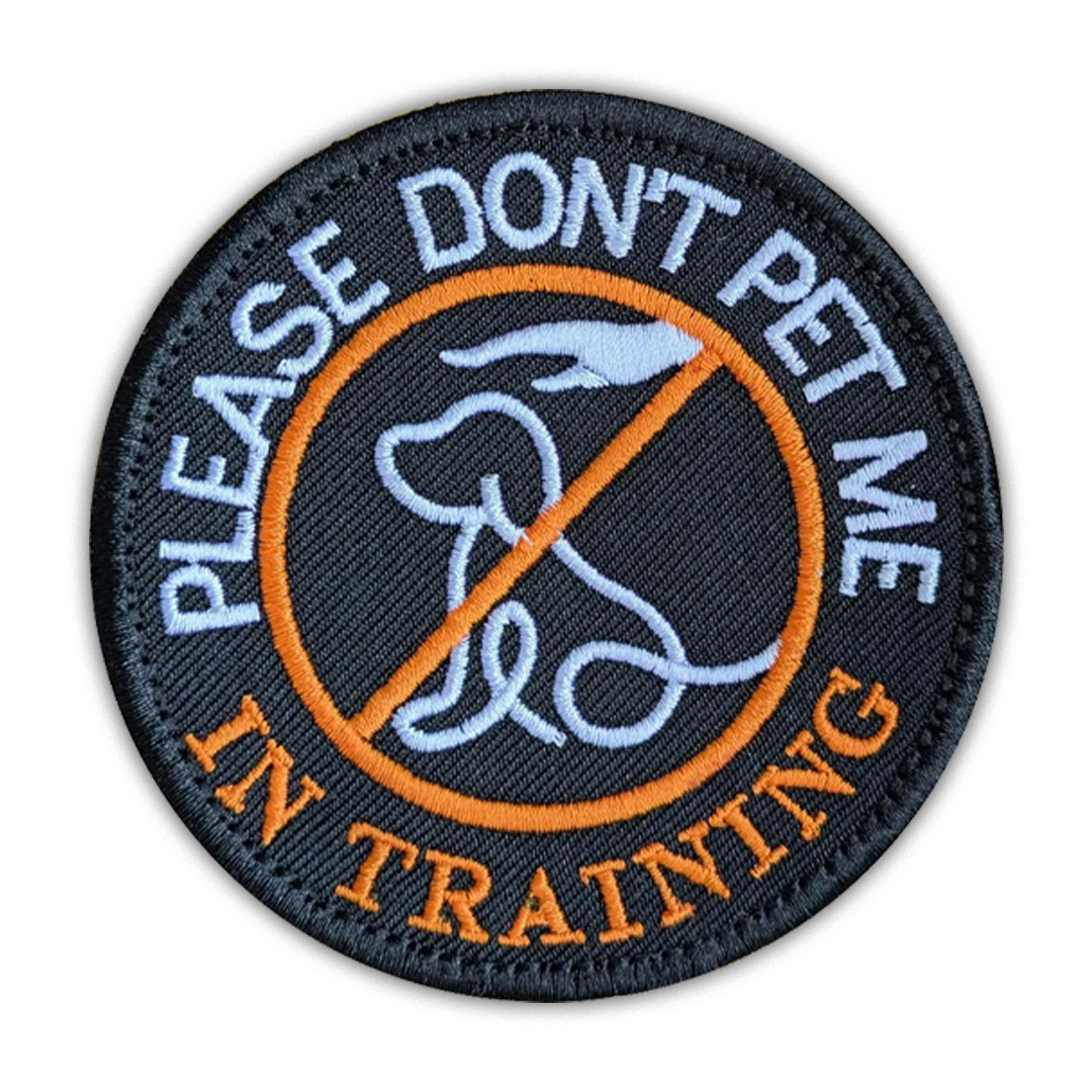 Round black service dog patch with orange border and text PLEASE DON'T PET ME IN TRAINING.